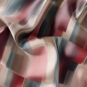 Peut inclure: Un tissu beige avec un motif abstrait coloré. Le motif présente des coups de pinceau dans des tons de rouge, rose, bleu et marron.