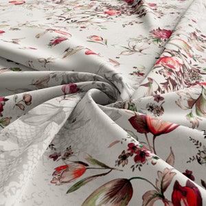 May include: White fabric with a floral print featuring red, pink, and green flowers. The fabric is folded and draped, showcasing the pattern.