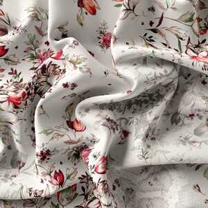 May include: White fabric with a floral print featuring red, pink, and green flowers. The fabric is draped and folded, showing the pattern.