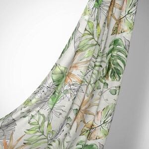May include: A white fabric with a green and orange tropical leaf pattern. The fabric is draped over a white background.