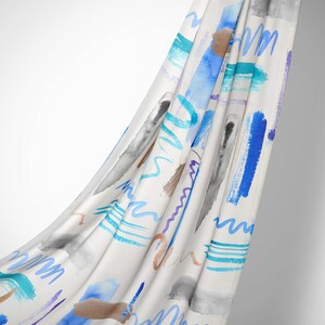 Op de afbeelding: Witte stof met een abstract aquarelpatroon in blauw, turquoise, paars en bruin. De stof is gedrapeerd en vloeit.