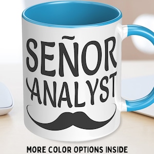 Op de afbeelding: Witte keramische koffiemok met een blauwe rand en handvat. De mok heeft een zwarte snor en de tekst "SEÑOR ANALYST" in zwart.