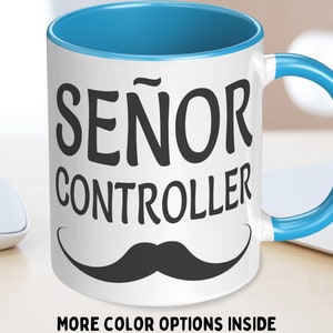 May include: White ceramic mug with a blue interior and handle. The mug features the words "SEÑOR CONTROLLER" in black, along with a black mustache graphic. The text "MORE COLOR OPTIONS INSIDE" is printed at the bottom.