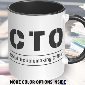 Op de afbeelding: Witte keramische mok met een zwarte rand en handvat. De mok heeft de tekst "CTO" in grote zwarte letters en de woorden "Chief Troublemaking Officer" in een kleiner lettertype eronder.