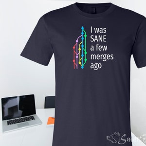 May include: Navy blue t-shirt with the text "I was SANE a few merges ago" in white. A colorful graphic of a branching diagram is on the left. The Smart Foxes logo is at the bottom right.