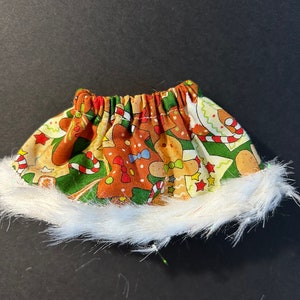 May include: A festive Christmas-themed skirt with a gingerbread man pattern in brown, green, and red. The skirt has a white faux fur trim at the bottom, creating a cozy and decorative look.