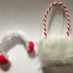 May include: A white fluffy Christmas ornament with a red and white twisted handle and red accents. The ornament has a soft, textured appearance, and is likely used for holiday decorations.