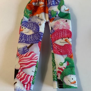 May include: Small, colorful pants with an elastic waistband, patterned with smiling snowmen wearing hats and scarves in various colors. The snowmen have carrot noses and are set against a white background.