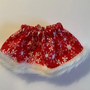 May include: Red and white fabric skirt with a snowflake pattern and a white fur trim.