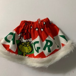 May include: A red and white fabric Christmas hat with a green Grinch graphic and the word "GRINCH" in green letters. The hat has a white faux fur trim around the bottom.