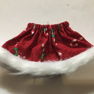 May include: Red and white Christmas-themed skirt with a white fur trim. The skirt has a pattern of candy canes and holly leaves.