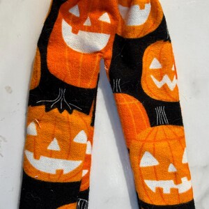 May include: Orange and black Halloween-themed pajama pants. The pants are covered in jack-o'-lantern faces with white cut-out features. The background is black. The pants have an elastic waistband.