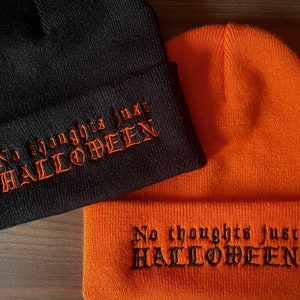 May include: Two knitted beanies are shown, one black and one orange. The black beanie has orange embroidered text that reads "No thoughts just HALLOWEEN." The orange beanie has black embroidered text that reads "No thoughts just HALLOWEEN."
