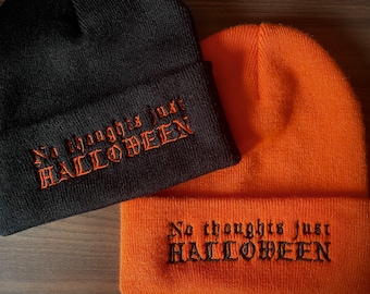 Könnte beinhalten: Zwei Strickmützen, eine schwarze und eine orangefarbene, werden gezeigt. Die schwarze Mütze hat einen orangefarbenen gestickten Text mit der Aufschrift "No thoughts just HALLOWEEN". Die orangefarbene Mütze hat einen schwarzen gestickten Text mit der Aufschrift "No thoughts just HALLOWEEN".