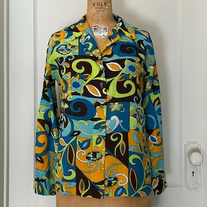 May include: A long-sleeved button-down shirt with a vibrant, retro floral pattern in shades of blue, green, orange, and brown. The shirt is displayed on a vintage mannequin with a size 10 label.
