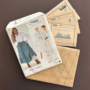 May include: A vintage Vogue sewing pattern for a skirt and blouse designed by Ralph Lauren. The pattern includes instructions and diagrams for sewing the garments. The pattern is in a brown envelope with the Vogue logo and the pattern number 2881.