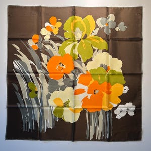 May include: A square brown scarf with a floral design. The flowers are in shades of orange, yellow, green, and white, with gray and white accents. The scarf is likely made of silk or a similar fabric.