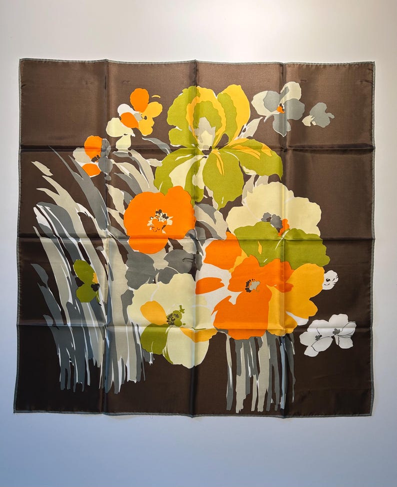 May include: A square brown scarf with a floral design. The flowers are in shades of orange, yellow, green, and white, with gray and white accents. The scarf is likely made of silk or a similar fabric.