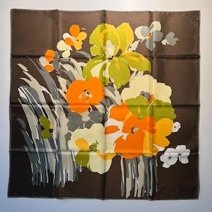 May include: Square silk scarf with a floral design. The scarf features a dark brown background with a bouquet of flowers in shades of orange, yellow, green, and white. The flowers are stylized with gray and white accents.