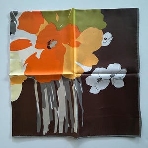 May include: A square silk scarf with a floral design. The scarf features large orange and yellow flowers against a dark brown background. The flowers have gray and white accents, and the scarf has a gray border.