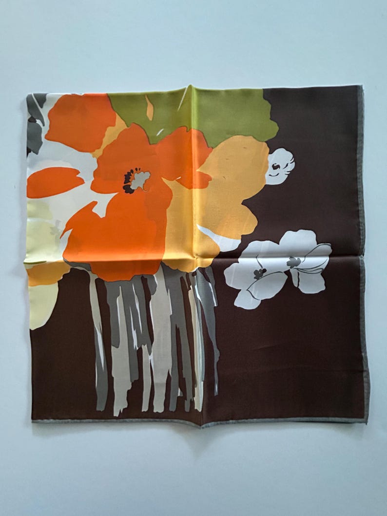 May include: A square silk scarf with a floral design. The scarf features large orange and yellow flowers against a dark brown background. The flowers have gray and white accents, and the scarf has a gray border.