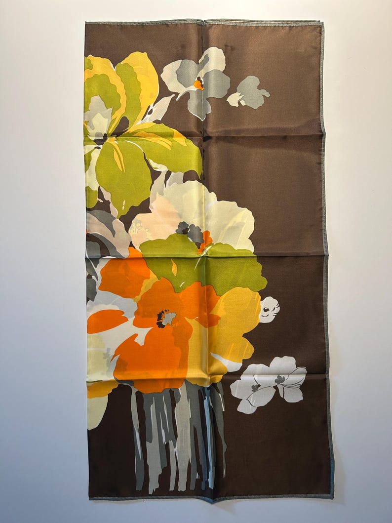 May include: A rectangular brown silk scarf with a floral design. The flowers are in shades of yellow, orange, white, and gray. The scarf has a dark brown border and a light gray trim.