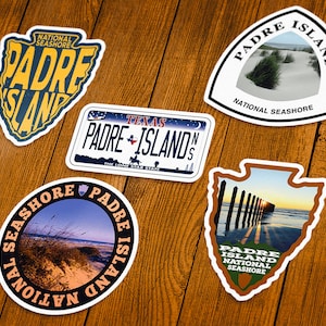 May include: A collection of five stickers featuring designs related to Padre Island National Seashore. The stickers include text and images of the beach, dunes, and a Texas license plate design. The color palette includes blue, yellow, brown, and white.