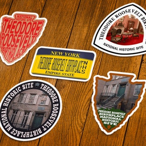 May include: A collection of stickers featuring the text "Theodore Roosevelt Birthplace" and "National Historic Site." The stickers have various shapes, including an arrowhead, a license plate, and a circle, with images of the birthplace.