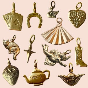 Könnte beinhalten: Eine Sammlung goldfarbener Anhänger, darunter ein Spielkartenblatt, ein Hufeisen, ein Schwan, ein Herz mit Blumendesign, eine Katze, ein Schwert, ein Fächer, ein Cherub, eine Erdbeere, eine Teekanne, ein Cowboy-Stiefel und ein Engel. Für Schmuck.