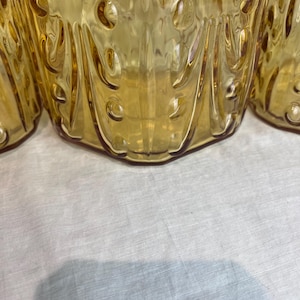 May include: Close-up of several amber-colored glass drinking glasses. The glasses have a textured, patterned design with rounded shapes and vertical lines. The glasses are on a white surface.