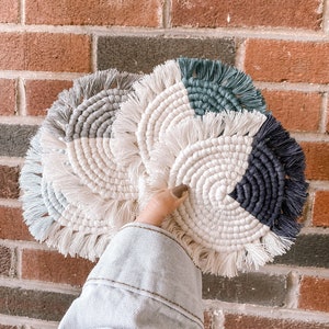 May include: Set of four crocheted coasters in a variety of colors, including white, gray, teal, and black. The coasters are circular and have a fringe border.