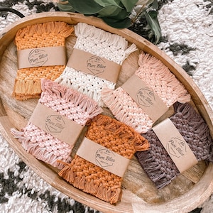 May include: Six crocheted coasters in a wooden tray. The coasters are in various colors, including brown, pink, white, and orange. Each coaster has a label that says "Pure Bliss" with a small flower design.