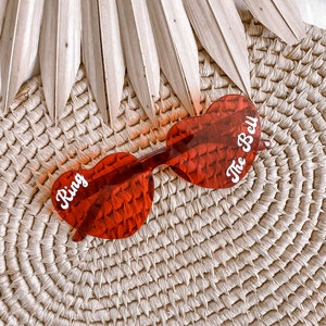 May include: Red heart-shaped sunglasses with the words "Ring" and "The Bell" written on the lenses.