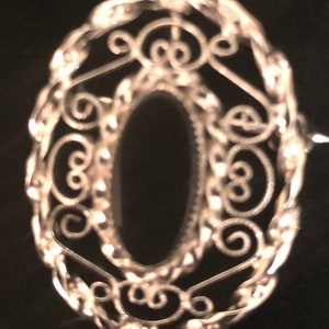 May include: A silver filigree oval ring setting with a black stone. The setting is made of delicate wire that is twisted and curled to create a decorative design.