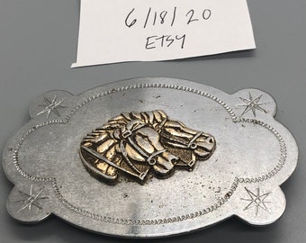 May include: Silver belt buckle with two gold horse heads in relief. The buckle has a star design on each side.