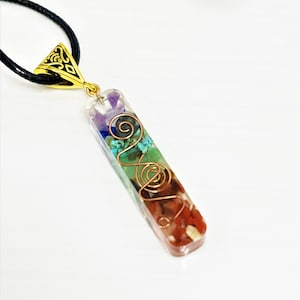 May include: A clear rectangular pendant with a gold-tone bail and a variety of colorful stones and copper wire swirls inside. The pendant is on a black cord.