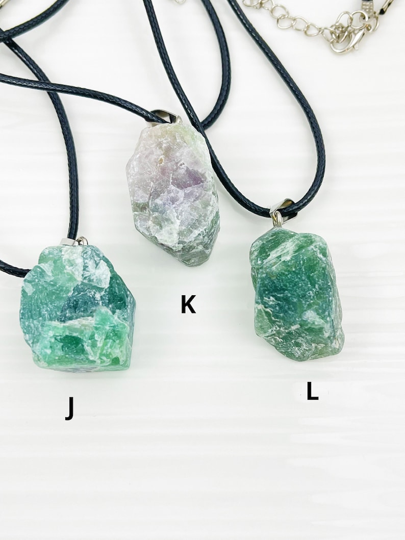 May include: Three necklaces with different green and purple crystal pendants. The pendants are all rough-cut and have a natural, organic look. The necklaces are labeled J, K, and L.