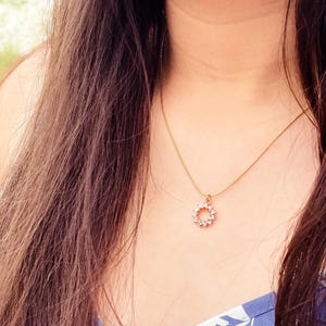 Pu&ograve; includere: Una collana d'oro con un piccolo ciondolo rotondo incastonato con pietre trasparenti. Il ciondolo ha la forma di un cerchio con un design delicato.