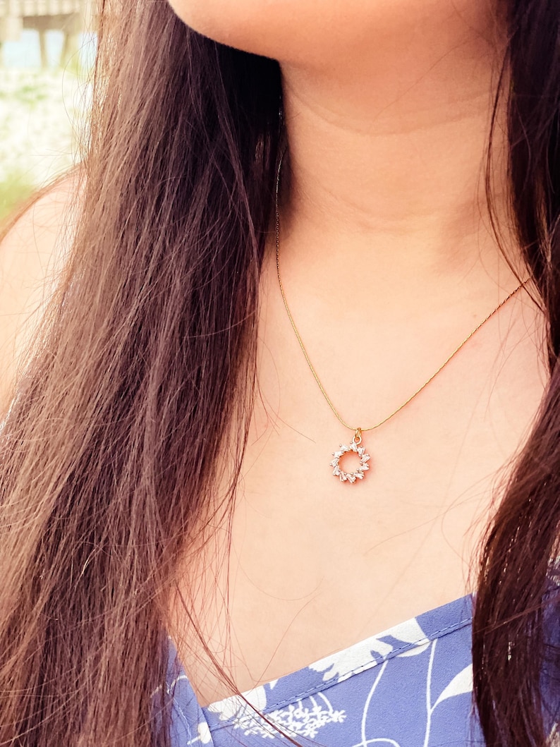 Pu&ograve; includere: Una collana d'oro con un piccolo ciondolo rotondo incastonato con pietre trasparenti. Il ciondolo ha la forma di un cerchio con un design delicato.