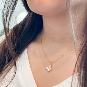 Pu&ograve; includere: Una collana con catena dorata e un ciondolo a forma di farfalla bianca. La farfalla ha un design delicato e femminile.