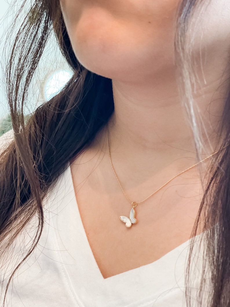 Pu&ograve; includere: Una collana con catena dorata e un ciondolo a forma di farfalla bianca. La farfalla ha un design delicato e femminile.