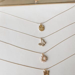 Pu&ograve; includere: Cinque collane d'oro con ciondoli diversi. La collana superiore ha un ciondolo rotondo con un motivo a farfalla. La seconda collana ha un ciondolo a farfalla. La terza collana ha un ciondolo circolare con piccole pietre. La quarta collana ha un ciondolo a farfalla. La quinta collana ha un ciondolo a farfalla.