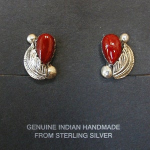 May include: A pair of sterling silver earrings with red coral stones and a leaf design. The earrings are handmade and feature a small silver bead on each side of the stone.
