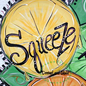 May include: A painted wooden door hanger with three citrus fruits, a lemon, an orange, and a lime. The lemon has the word "Squeeze" written in black with white dots on it. The background is black and white stripes with a red and white pattern.