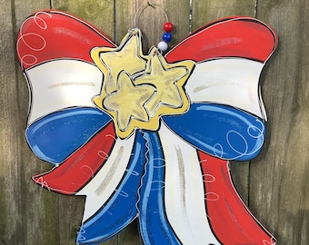 May include: A red, white, and blue bow with gold stars, perfect for a patriotic door decoration.