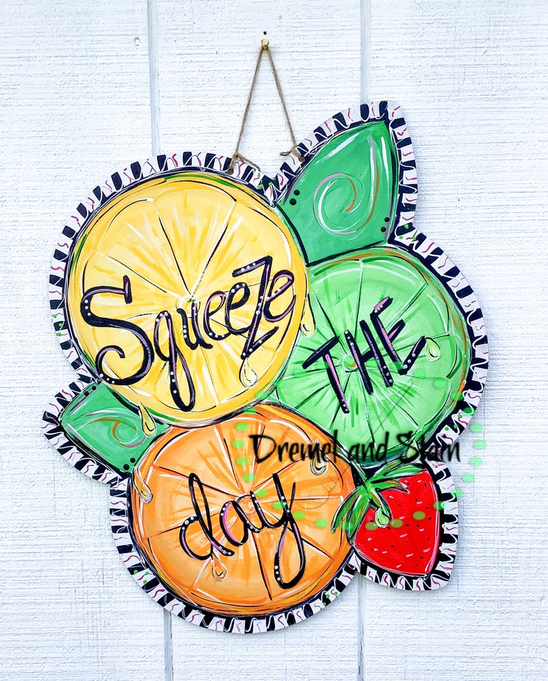 May include: A wooden door hanger with a painted design of lemons, limes, and an orange. The text "Squeeze the day" is written in black paint. A strawberry is painted in the bottom right corner.