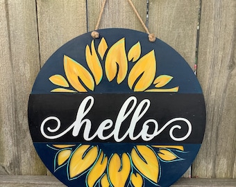 May include: A round wooden sign with a blue background and a yellow sunflower design. The sign says "hello" in white lettering.