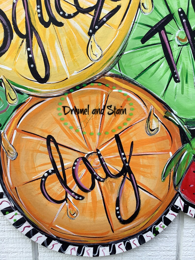 May include: A painted wooden door hanger with a citrus theme. The hanger features a large orange slice with the word "day" written in black script. The orange slice is surrounded by lemons and lime slices, all with painted details of leaves and dripping juice.