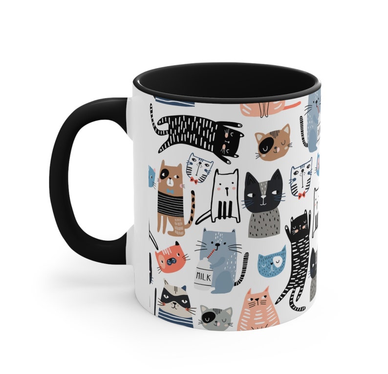 May include: A white ceramic coffee mug with a black handle and black interior. The mug features a repeating pattern of colorful cartoon cats in various poses.