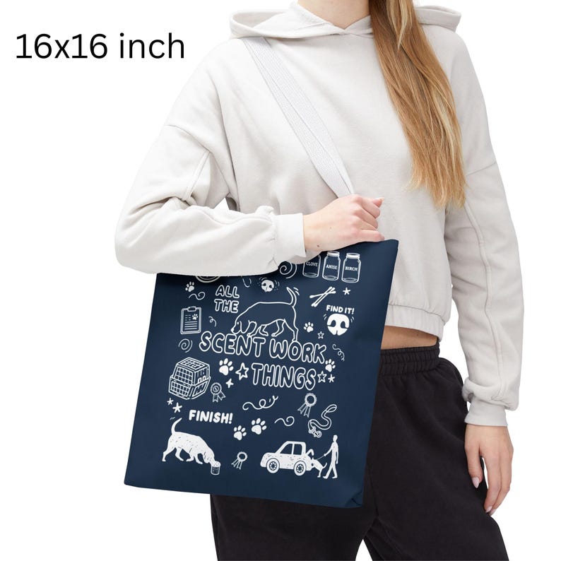 May include: A navy blue tote bag, measuring 16x16 inches, features white illustrations and text related to scent work. The design includes dog silhouettes, paw prints, and the phrases "ALL THE SCENT WORK THINGS" and "FIND IT!".